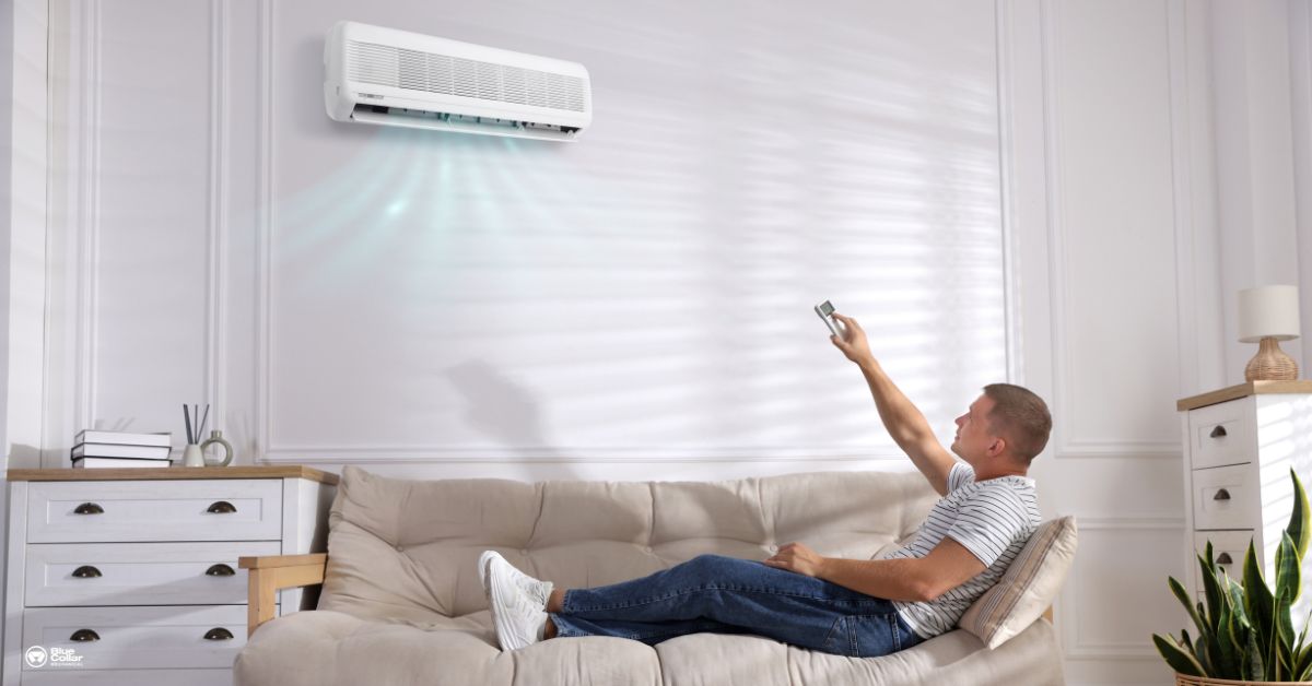 male sitting on couch at home, turning up the AC since it's a hot day outside